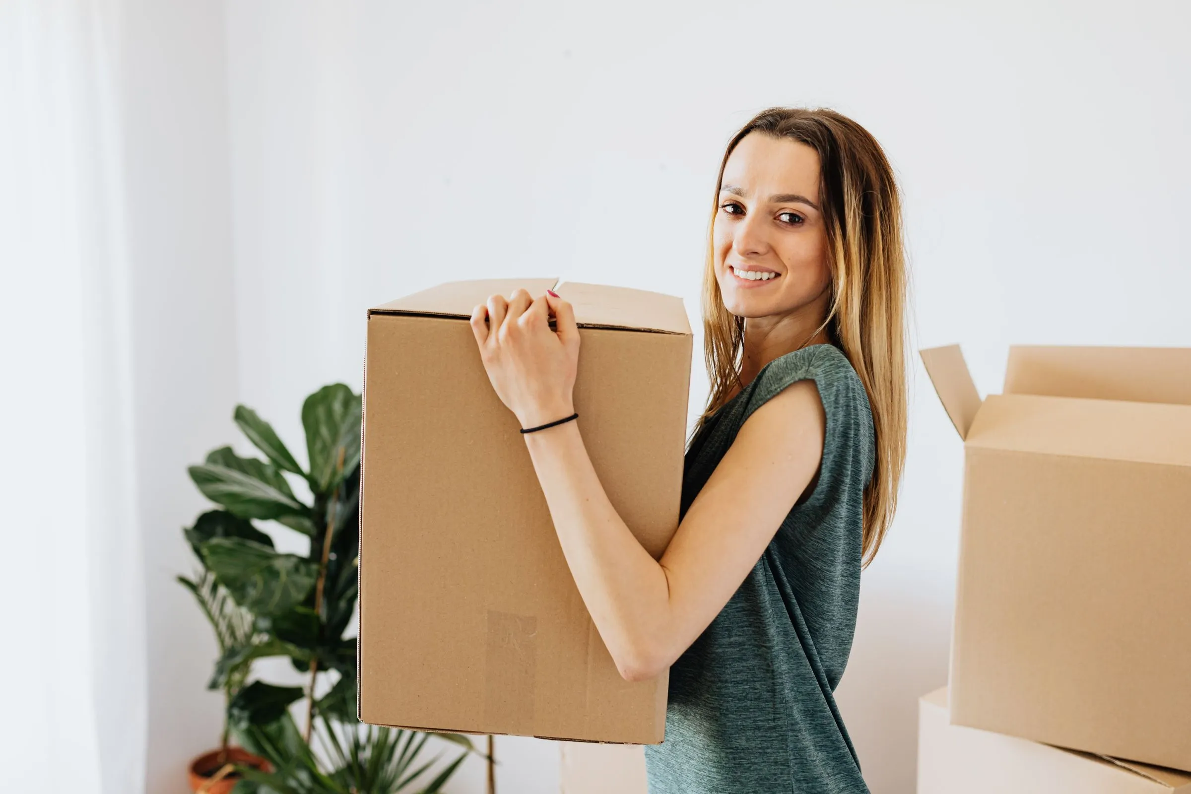 Chica joven llevando una caja de mudanza en su nueva casa